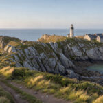 Vue panoramique du littoral finistérien avec un sentier côtier, un phare breton et un village baigné par une lumière douce.